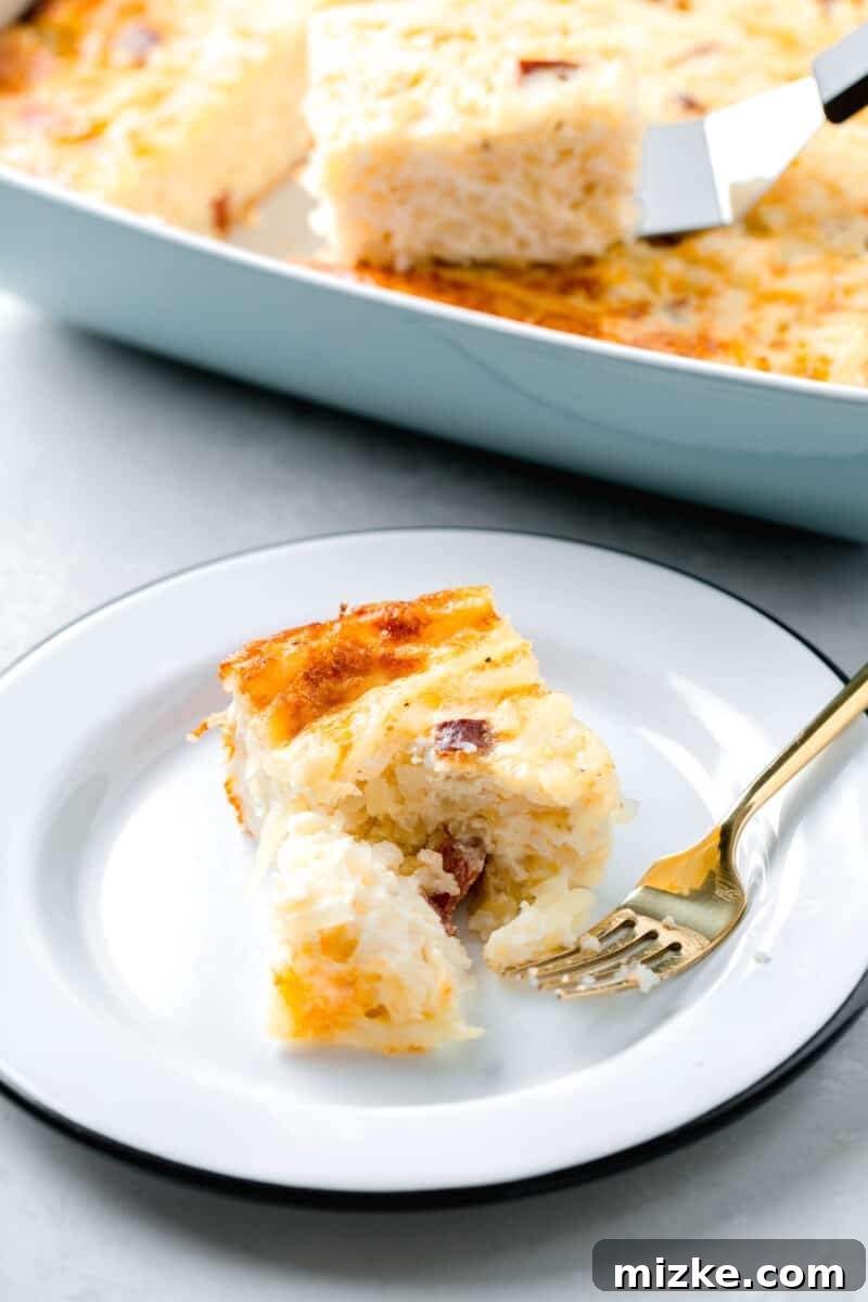 A delectable slice of egg white breakfast casserole on a pristine white plate with a black rim, elegantly accompanied by a shining gold fork, showcasing its fluffy texture and inviting, golden-brown appearance.