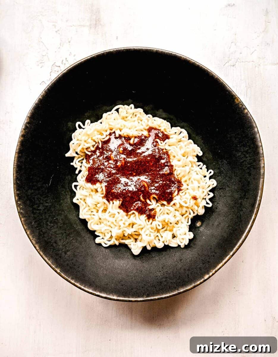 Instant ramen noodles are coated in a full-flavored, spicy sauce in this delicious, quick, and easy buldak ramen recipe. The buldak ramen sauce being added generously to the freshly cooked and drained ramen noodles.