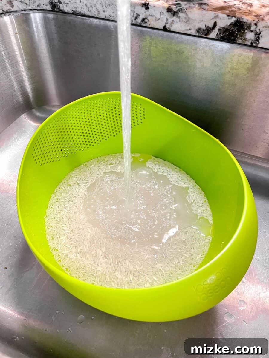 Perfect Instant Pot Jasmine Rice 4 Water running over uncooked jasmine rice in a bright green colander, showing the rinsing process