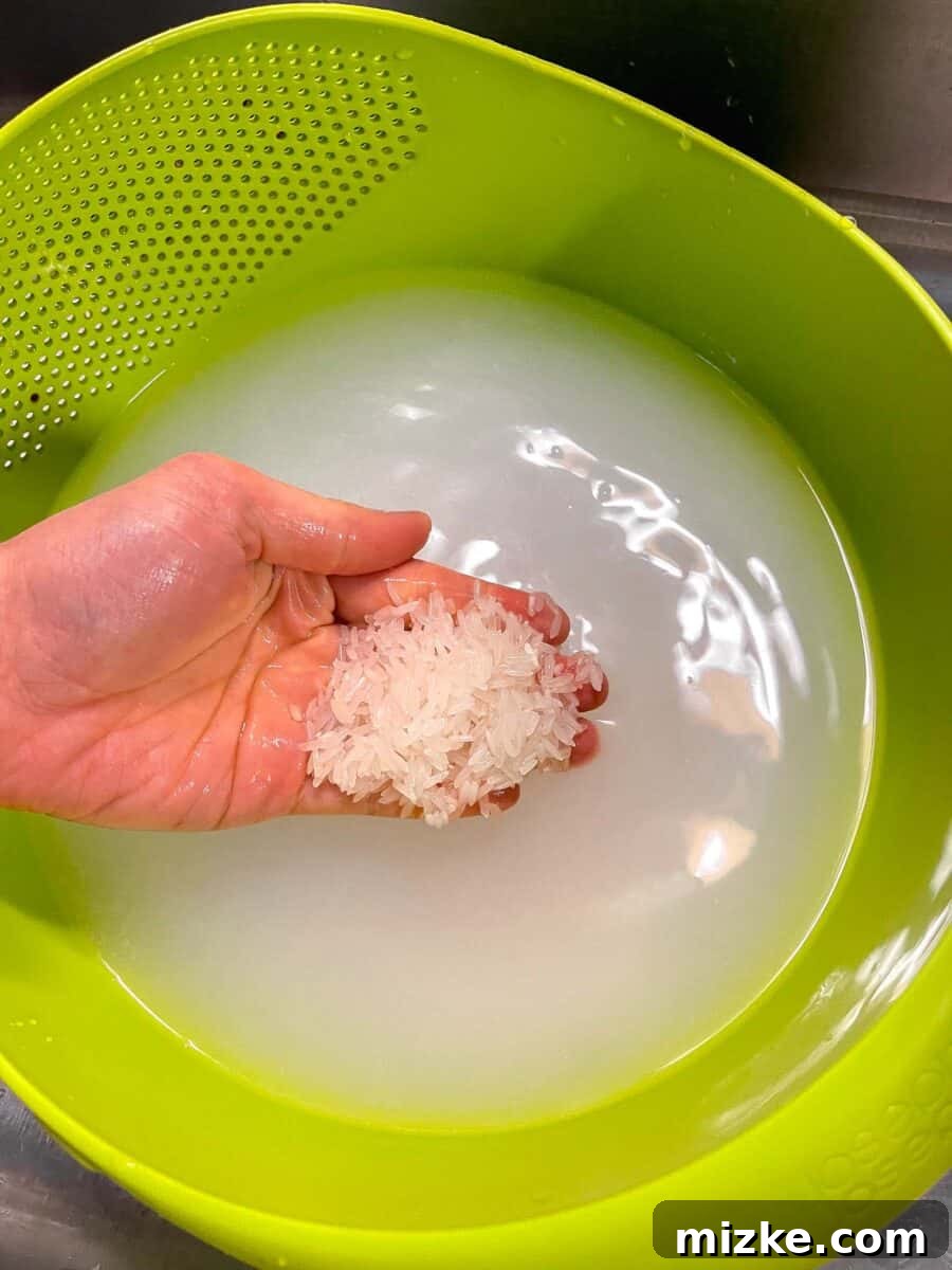 Perfect Instant Pot Jasmine Rice 5 A hand holding washed jasmine rice in a bright green colander, with cloudy starchy water below