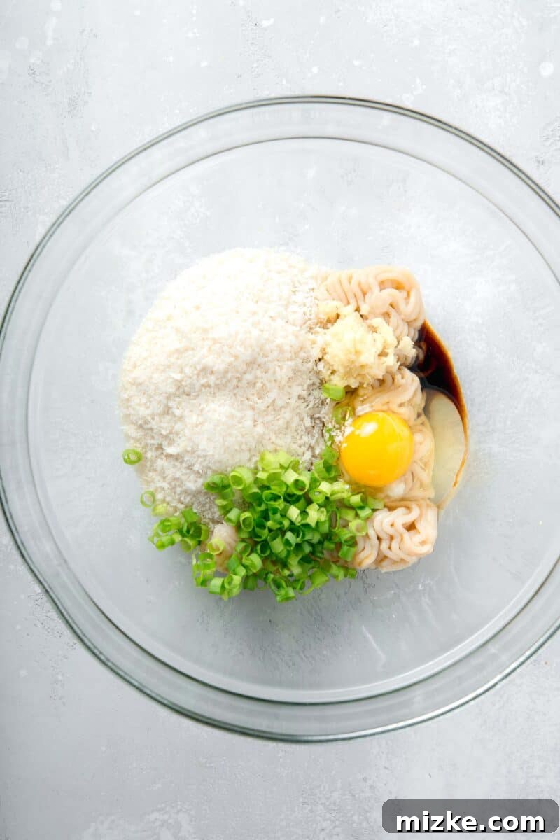 The foundation for homemade juicy teriyaki chicken meatballs: ground chicken expertly blended with grated ginger, salty soy sauce, and other key seasonings. All the essential ingredients for teriyaki chicken meatballs meticulously arranged in a spacious clear mixing bowl, ready for combining.