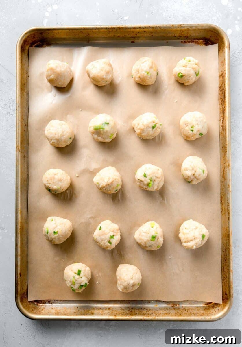 Evenly shaped meatballs, a perfect blend of ground chicken, grated ginger, salty soy sauce, and more, ready for the oven to become juicy teriyaki chicken meatballs. Precisely formed teriyaki chicken meatballs, arranged neatly on parchment paper atop a rimmed baking sheet, poised for baking.