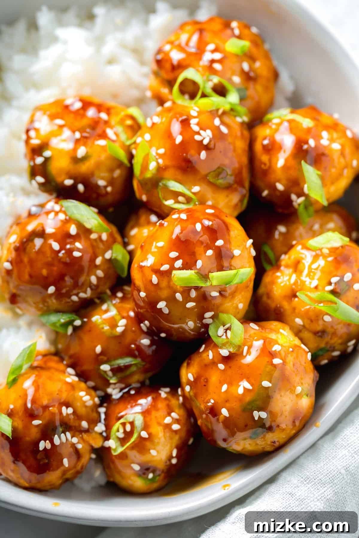 An up-close view of perfectly cooked ground chicken meatballs, richly flavored with grated ginger and salty soy sauce, and generously coated in glossy teriyaki sauce. A close-up, mouth-watering image of beautifully glazed teriyaki chicken meatballs, garnished with vibrant fresh scallions and tiny sesame seeds, highlighting their irresistible texture and coating.