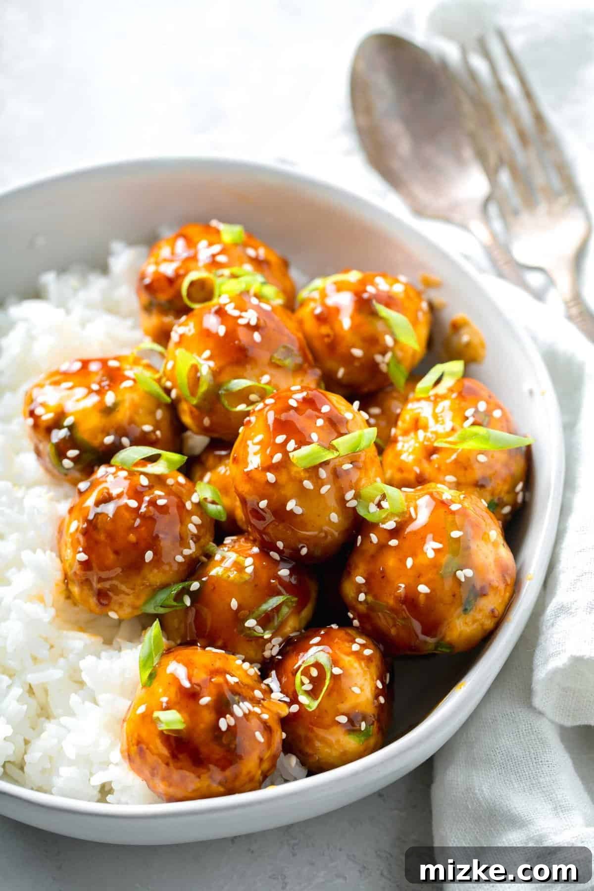 A perfectly composed dish of ground chicken meatballs, expertly seasoned with grated ginger and salty soy sauce, and coated in a delicious teriyaki glaze, served with rice. Another inviting view of teriyaki chicken meatballs, beautifully glazed and garnished with fresh scallions and sesame seeds, presented in a bowl with white rice, next to a neat linen napkin.