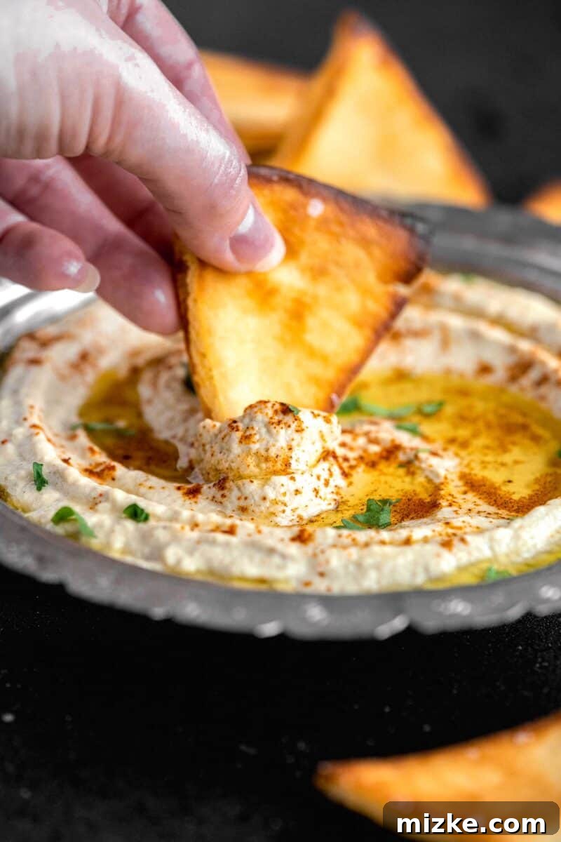 Smoky and Simple Baba Ganoush 12 A hand dipping a crispy pita chip into a beautifully textured bowl of Baba Ganoush, highlighting its creamy consistency.