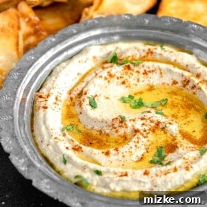 A bowl of Authentic Easy Baba Ganoush, garnished with fresh parsley, a drizzle of olive oil, and a sprinkle of cayenne pepper.