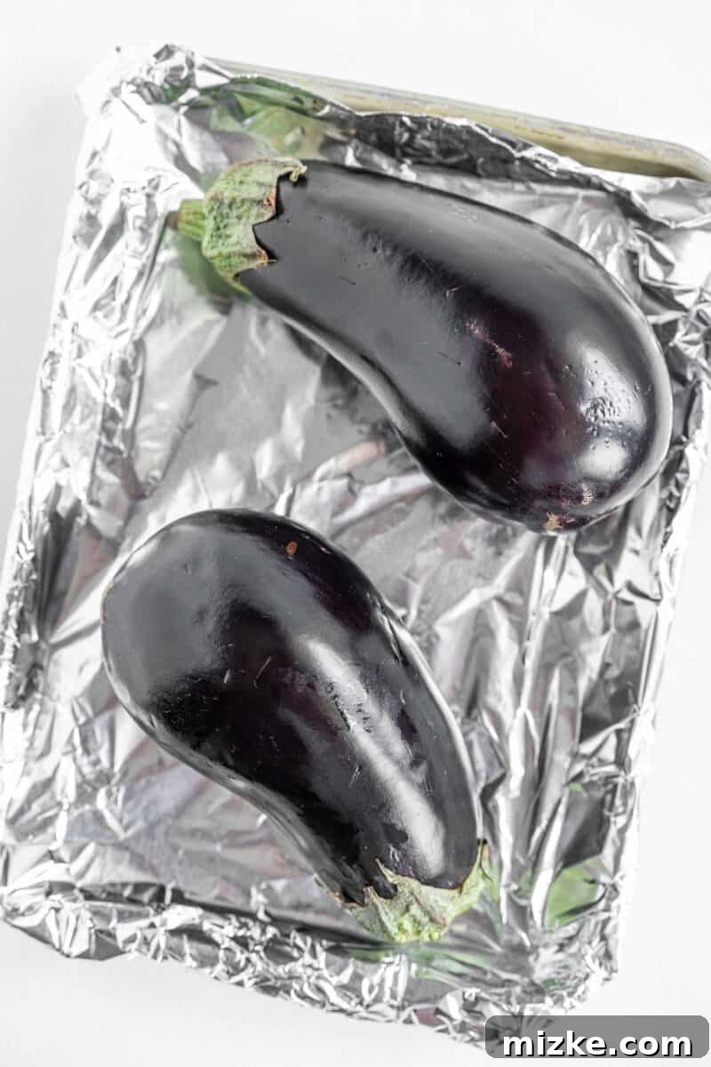 Smoky and Simple Baba Ganoush 4 Two raw, unroasted eggplants placed on a foil-lined baking sheet, ready for preparation.