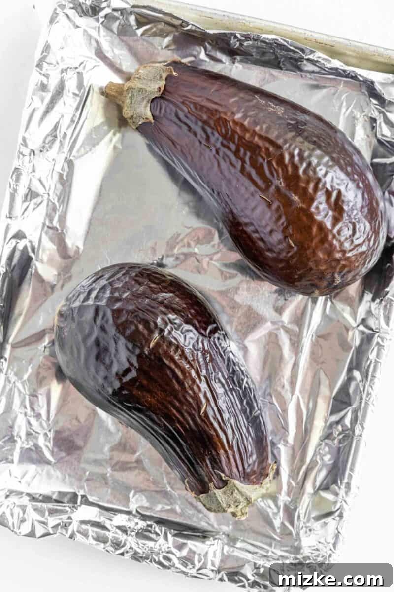 Smoky and Simple Baba Ganoush 5 Two perfectly roasted eggplants, their skins wrinkled and slightly charred, resting on a baking sheet after being removed from the oven.