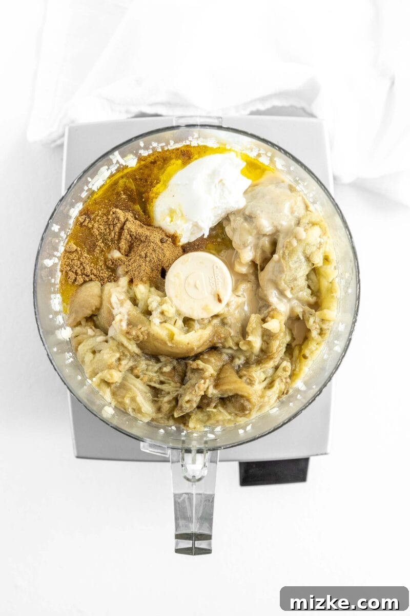 Smoky and Simple Baba Ganoush 8 All the Baba Ganoush ingredients, including roasted eggplant, tahini, lemon juice, and garlic, assembled in a food processor bowl, ready for blending.