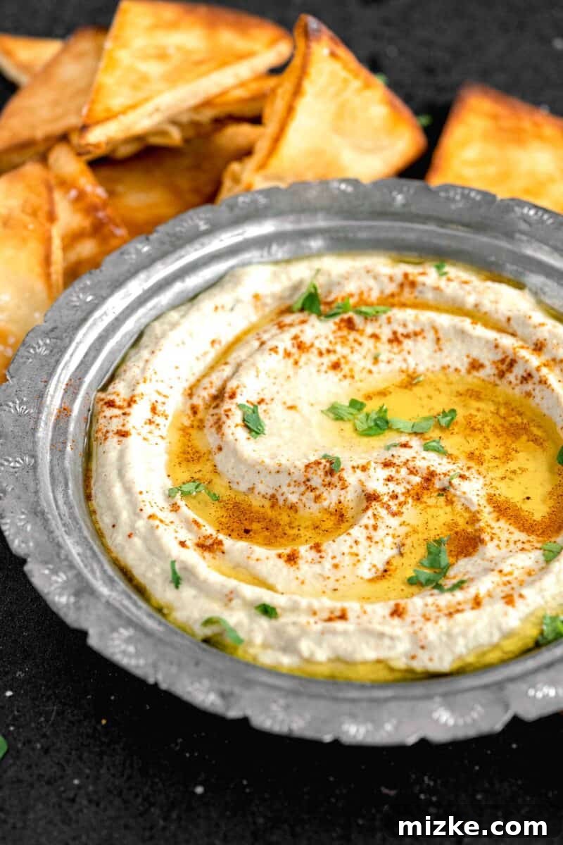 Smoky and Simple Baba Ganoush 10 A close-up of a bowl of Baba Ganoush elegantly garnished with fresh parsley, a drizzle of olive oil, and a sprinkle of vibrant cayenne pepper.