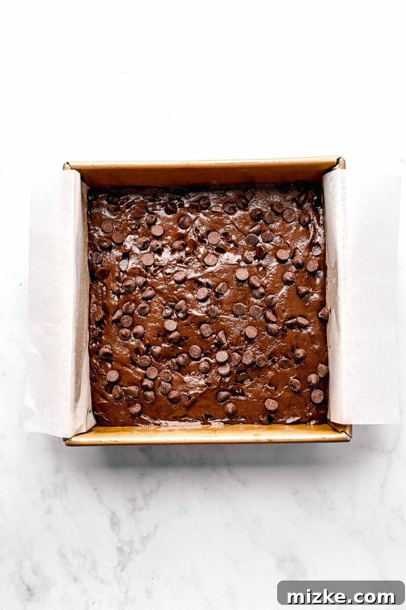These cake mix brownies turn baking into a walk in the park. Made with 5 ingredients in 30 minutes, they're sure to become a new favorite. Chocolate chip-filled brownie batter spread evenly in a parchment paper-lined brownie pan, ready for the oven.