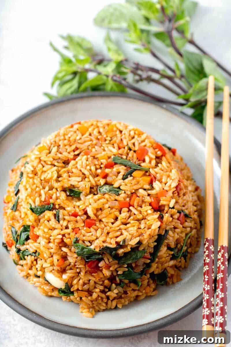 thai basil fried rice in a bowl mold on top of a grey ceramic plate with wooden chopsticks and thai basil next to the plate
