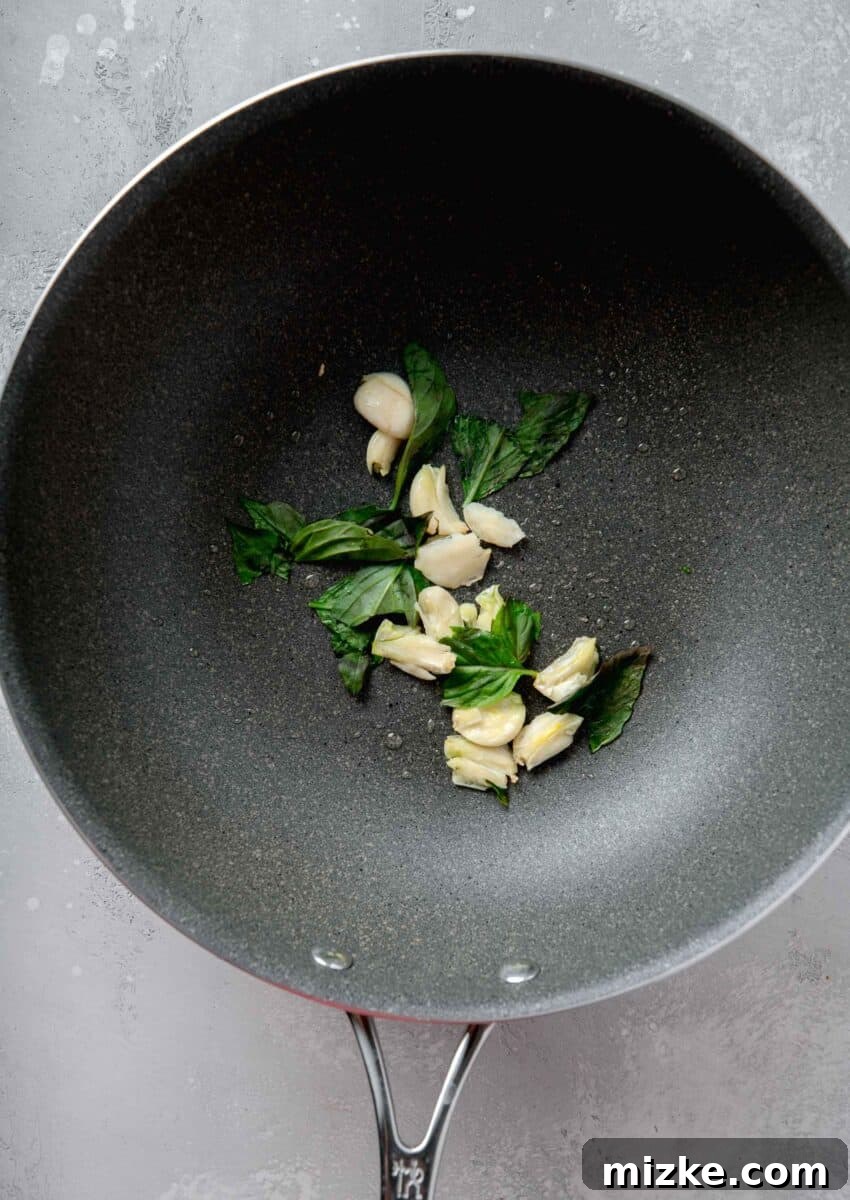 smashed garlic and thai basil in a grey nonstick skillet