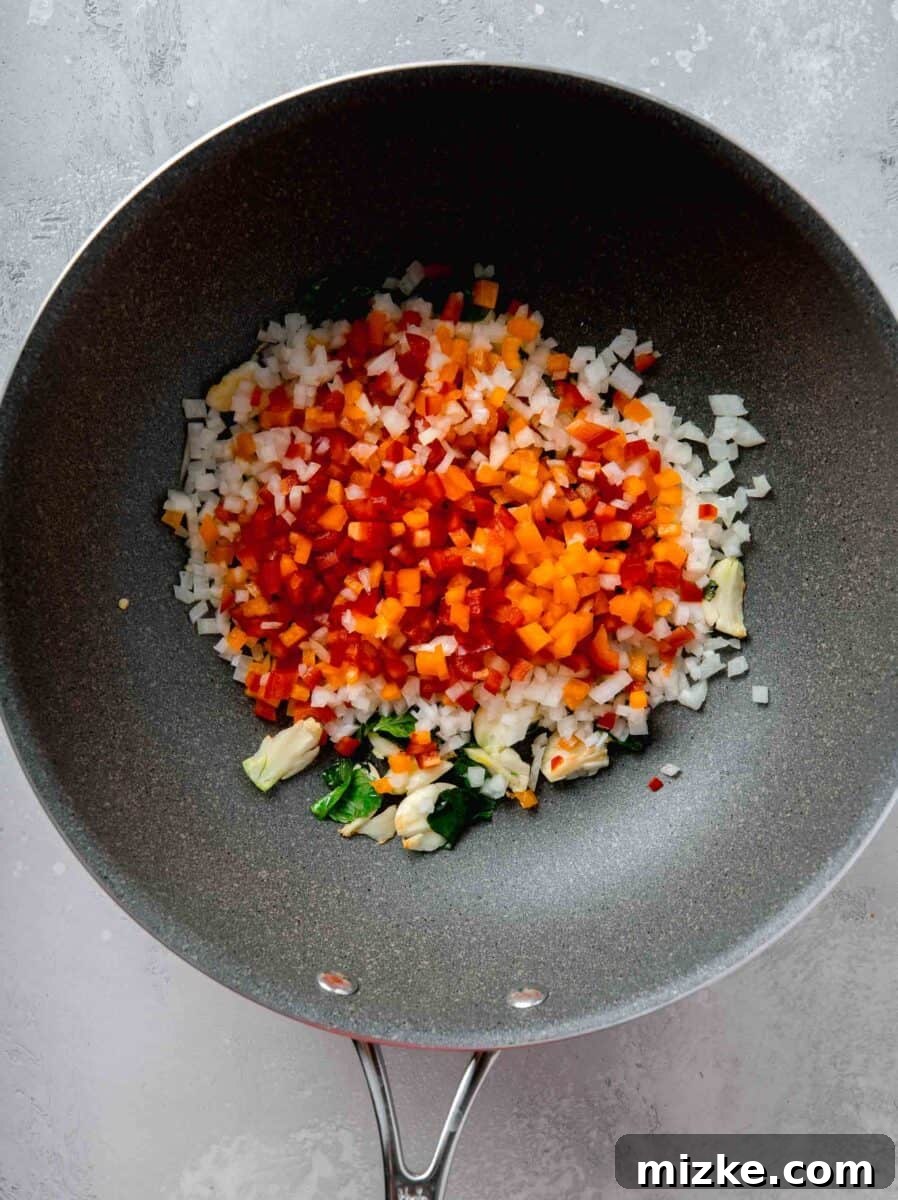 red and orange diced bell peppers and diced onions added to the nonstick skillet with the garlic and thai basil