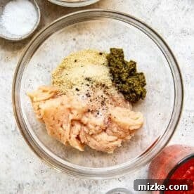 Ground chicken, pesto, panko breadcrumbs, salt, and pepper combined in a clear bowl, ready to be mixed into meatballs.