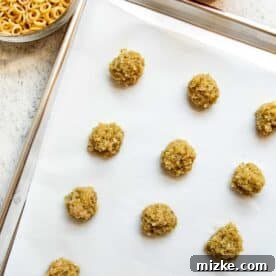 Small, rolled chicken pesto meatballs neatly arranged on a parchment paper-lined metal baking sheet before baking.