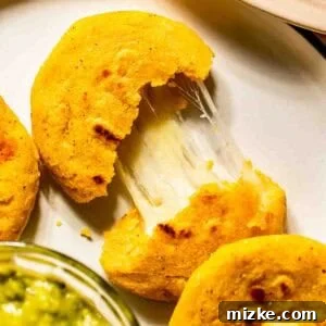 Gooey Cheese Pupusas 4 A cheese-stuffed pupusa is split open on a plate, showing melted cheese inside. A bowl of green sauce is visible in the foreground.