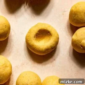 Gooey Cheese Pupusas 8 Several round yellow dough balls are arranged on a light surface, with one dough ball in the center showing an indentation.