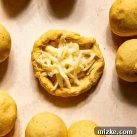 Gooey Cheese Pupusas 9 Round dough balls surround one open dough piece filled with shredded cheese on a light surface.