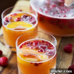 Close-up of the delicious Raspberry Peach Prosecco Punch ready to be served in a elegant pitcher with garnishes.