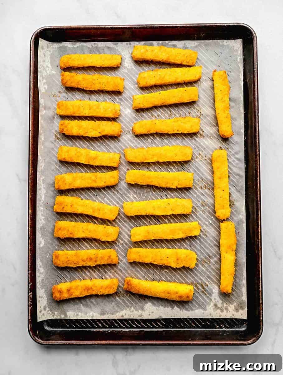 These polenta fries are made from cheesy polenta cut into strips, brushed with olive oil, and baked to crispy golden brown. Baked polenta fries on a baking sheet lined with parchment paper.