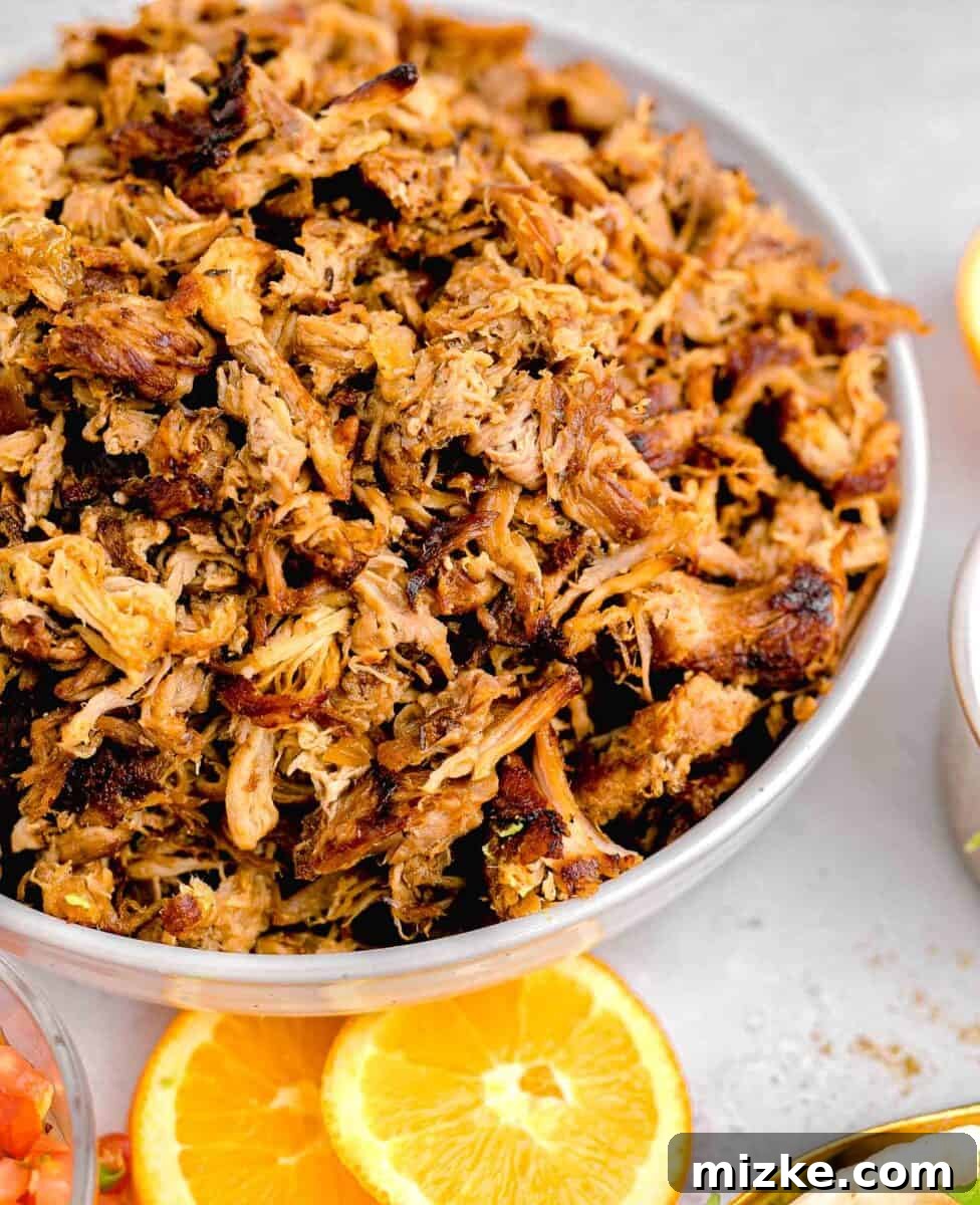 Melt-Away Slow Cooker Pork Carnitas 2 Two orange slices are placed next to a bowl of perfectly cooked, shredded carnitas, ready to be served.