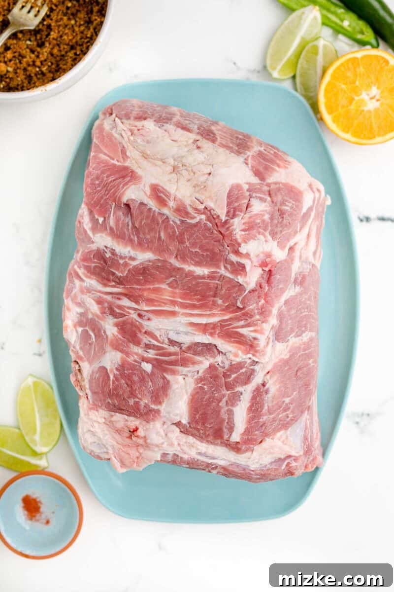 Melt-Away Slow Cooker Pork Carnitas 6 A large piece of uncooked pork butt is placed on a blue cutting board, ready for seasoning.