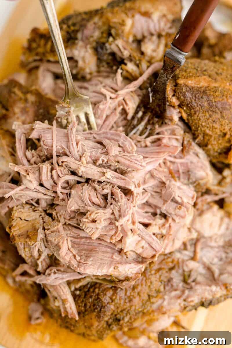 Melt-Away Slow Cooker Pork Carnitas 10 Tender, cooked pork is being expertly shredded with two forks on a cutting board.