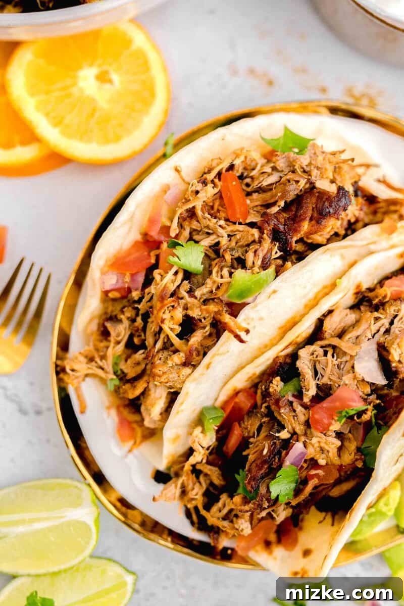 Bright orange halves are artfully arranged next to a plate holding two delicious pork carnitas street tacos.