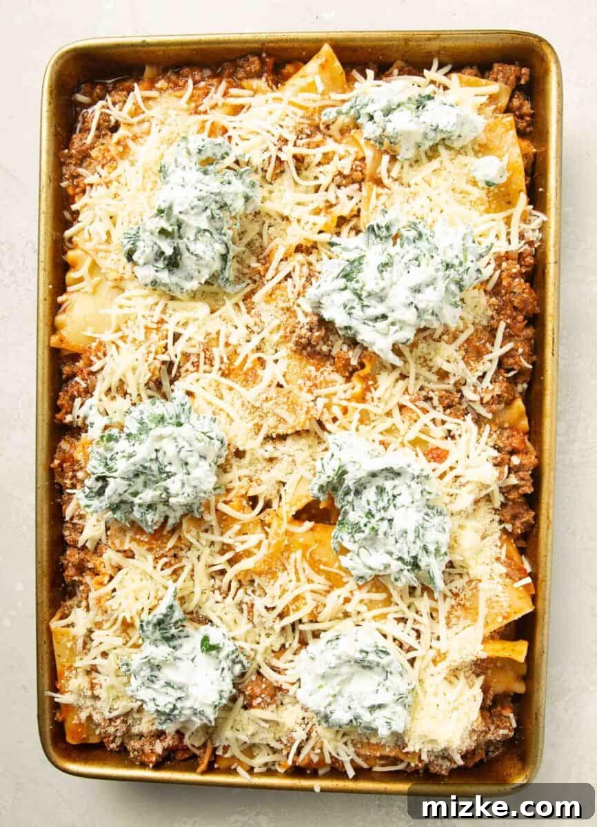 Effortless Sheet Pan Lasagna 11 assembled sheet pan lasagna on a metal rimmed baking sheet with ricotta and spinach dollops on top