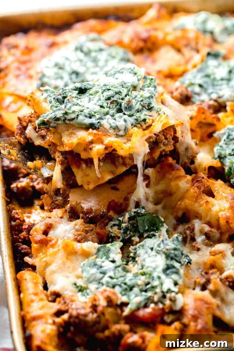 Effortless Sheet Pan Lasagna 12 sheet pan lasagna piece on a metal spatula hovering above the sheet pan, showing a perfectly cooked portion
