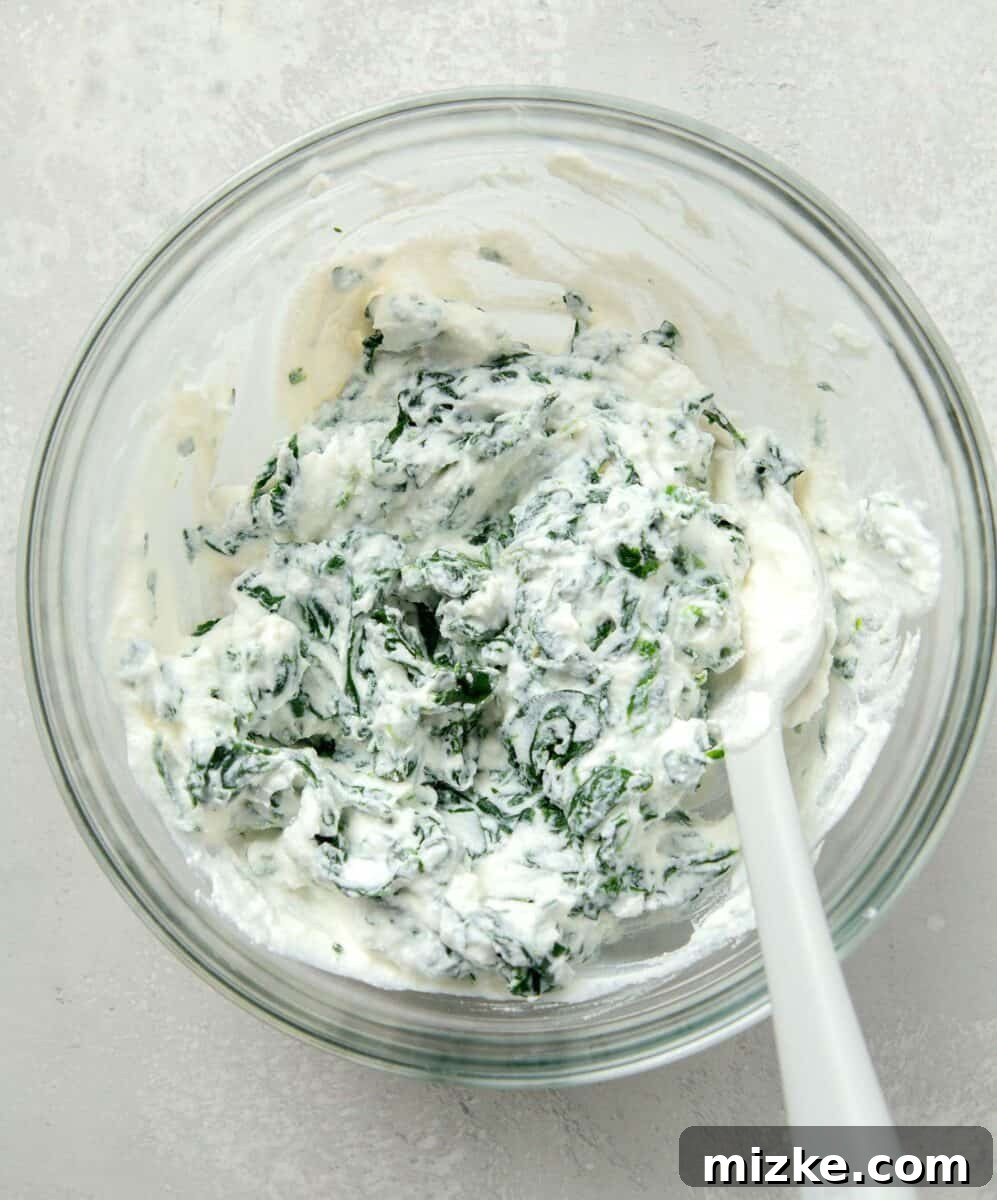 Effortless Sheet Pan Lasagna 5 ricotta and spinach mixed together in a clear bowl with a silicone spoon