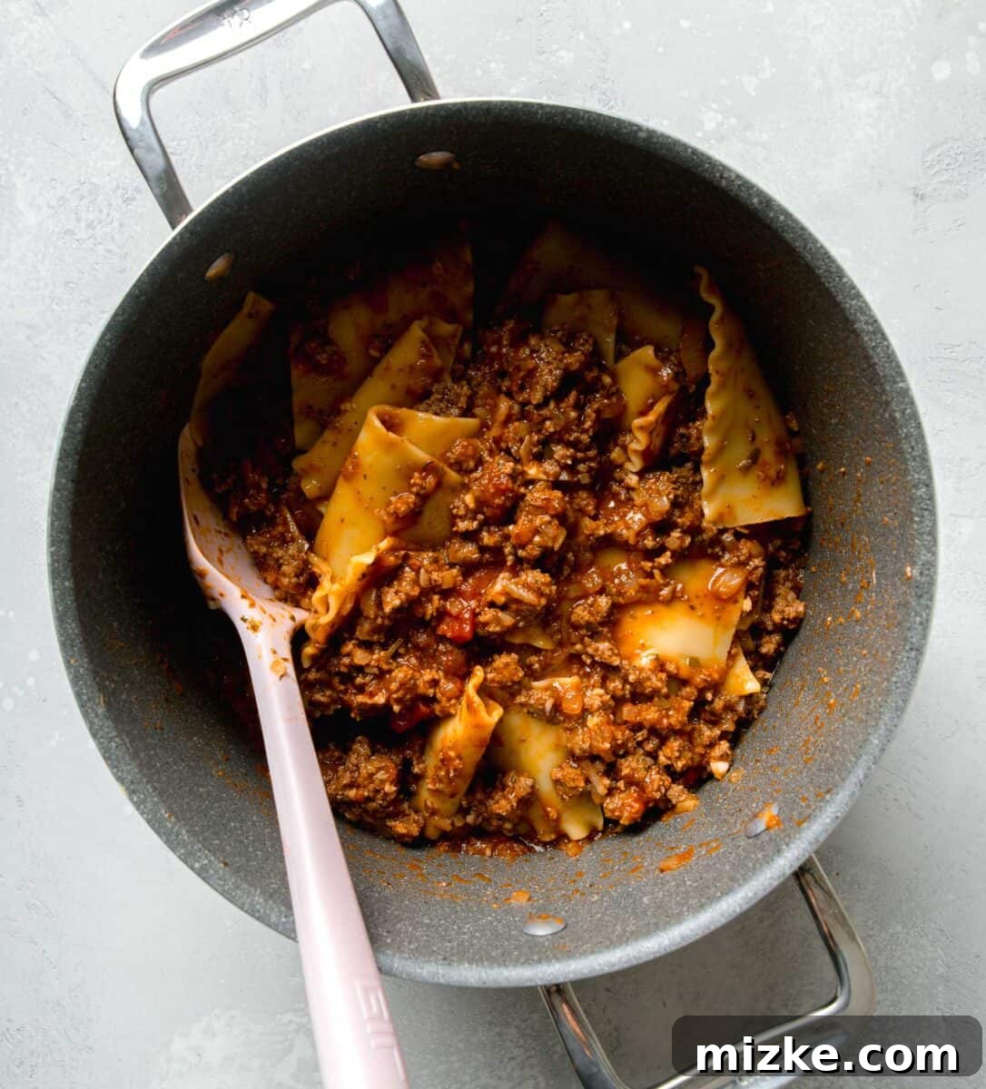 Effortless Sheet Pan Lasagna 9 lasagna noodles with beef mixture and marinara sauce all mixed together in a large pot with a pink silicone spatula