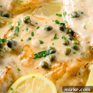 Chicken breasts in a creamy lemon sauce with fresh parsley and capers on top next to a lemon wedge