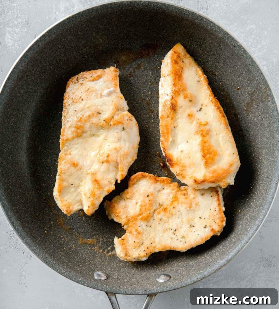 Velvety Lemon Chicken Piccata 6 Golden-brown, thinly sliced chicken breasts perfectly seared and resting in a large grey nonstick skillet, awaiting the addition of the creamy lemon sauce.