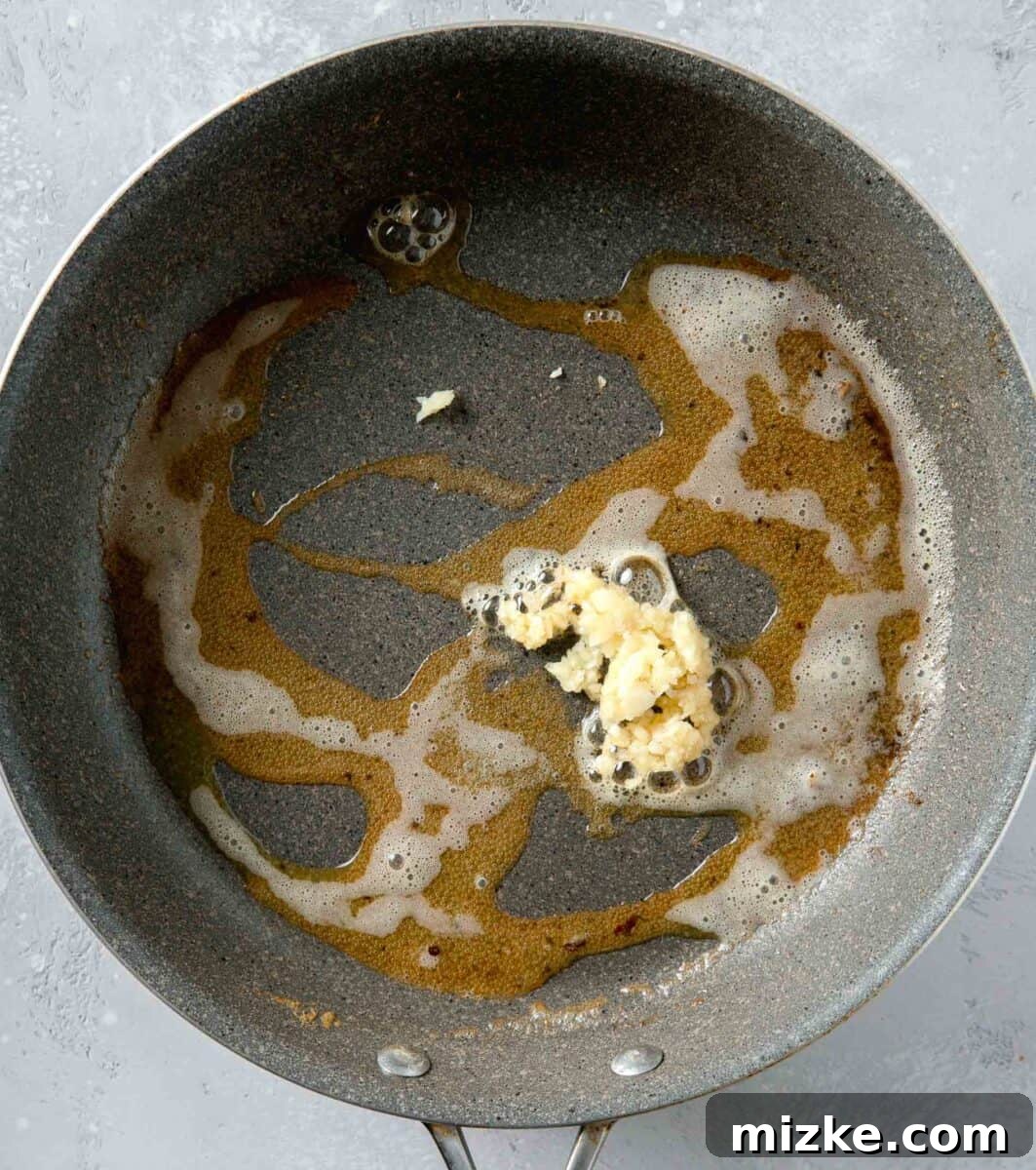 Velvety Lemon Chicken Piccata 7 Minced garlic being added to melted butter in a nonstick skillet, beginning the aromatic foundation for the creamy lemon sauce.