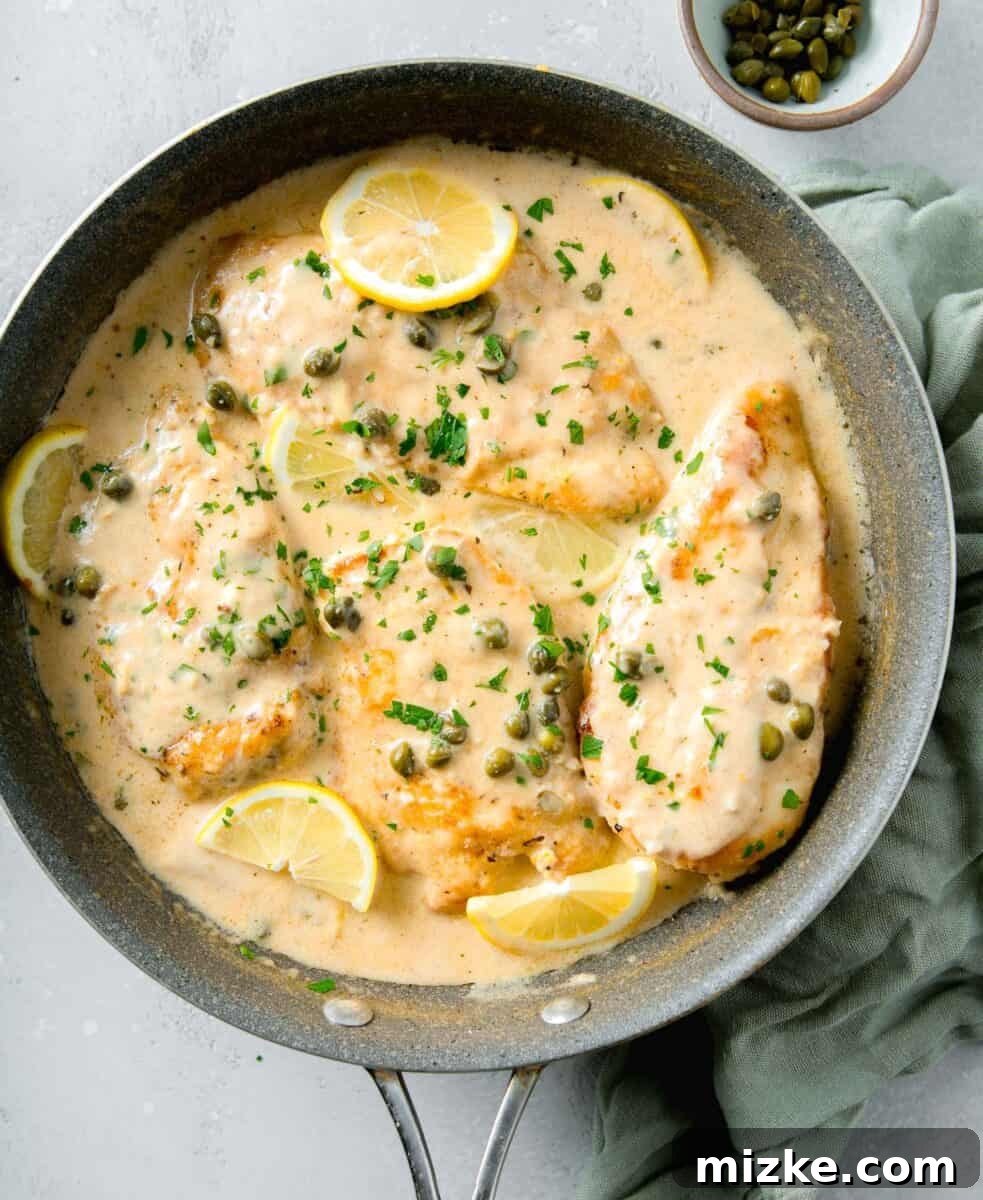 Velvety Lemon Chicken Piccata 9 An overhead view of four beautifully browned chicken breasts submerged in a creamy lemon sauce, elegantly topped with fresh parsley, briny capers, and garnished with vibrant lemon slices, ready to be served.