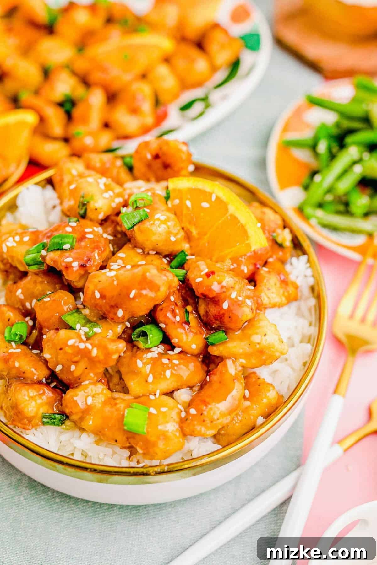 Experience the ultimate homemade orange chicken: crispy, juicy, and coated in the best orange sauce ever. A bowl of homemade orange chicken over fluffy white rice, garnished with green onions and sesame seeds.