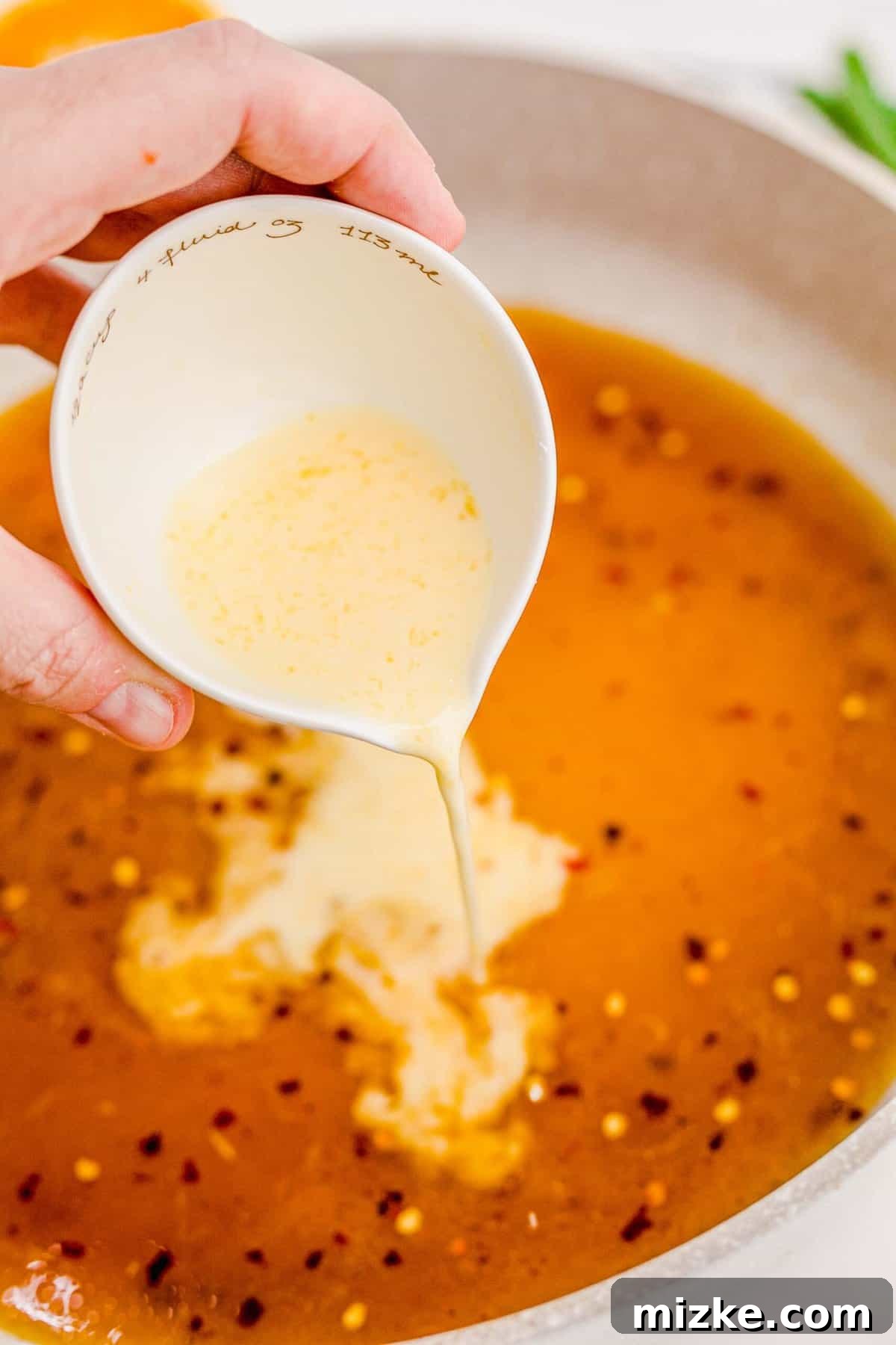 Achieving the ideal thick consistency for your orange chicken sauce. Mixing the cornstarch slurry into the simmering orange chicken sauce in the skillet to thicken it.