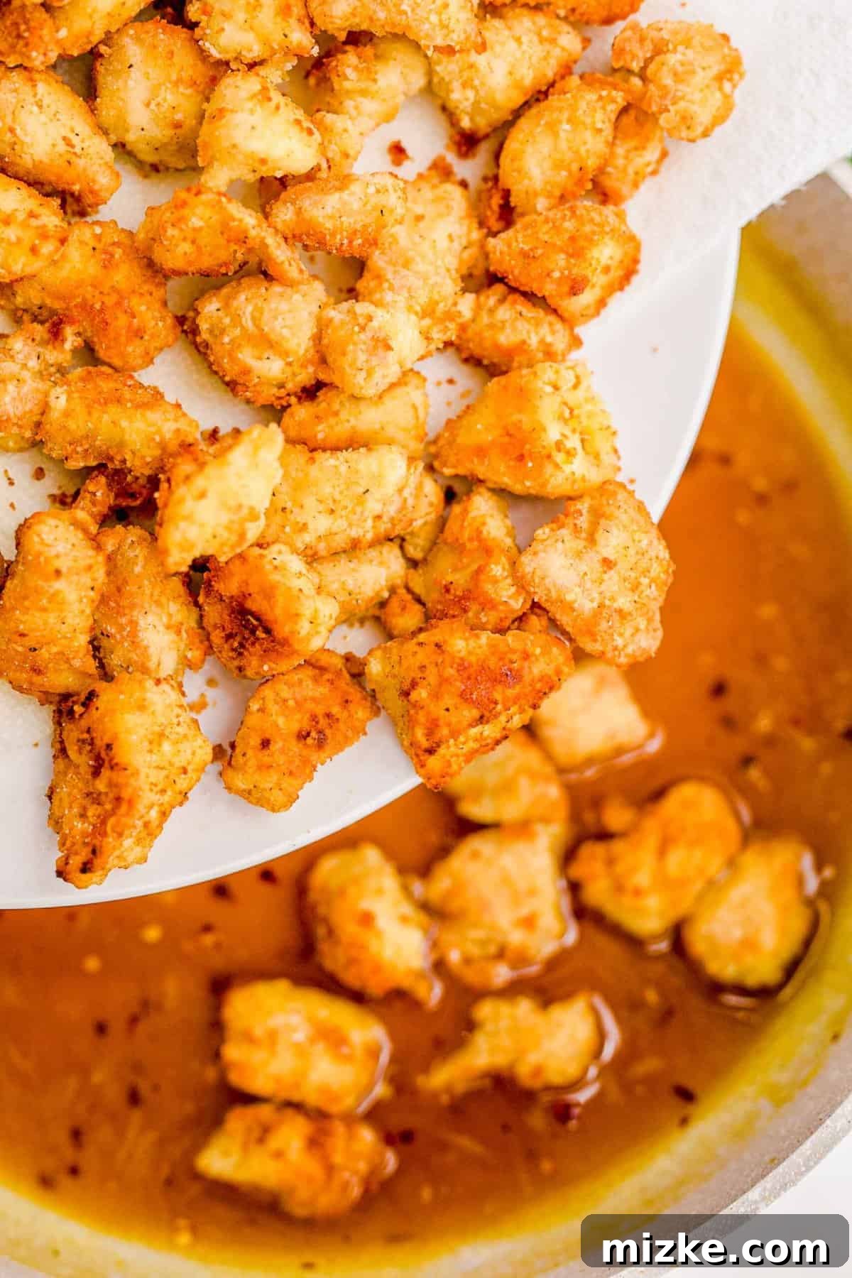 Tossing crispy chicken in the rich homemade orange sauce. Adding the golden-brown fried chicken pieces back into the simmering orange sauce in the skillet.