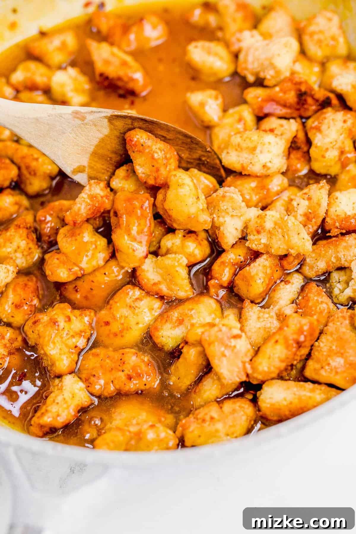 The exquisite result: every piece of chicken perfectly coated and ready to serve. Close-up of perfectly coated orange chicken, glistening with thick, tangy sauce in the skillet.