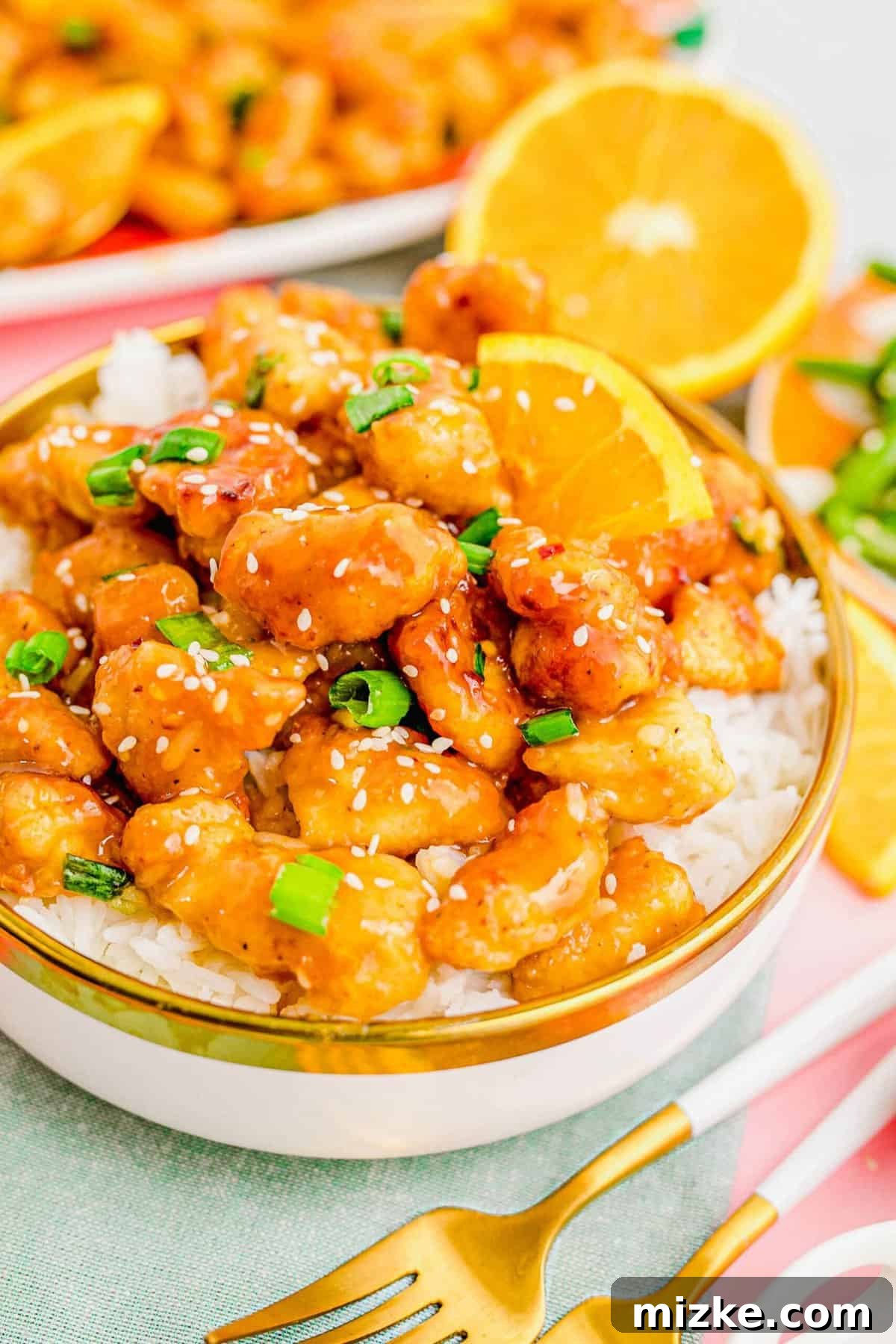 The ultimate homemade orange chicken: vibrant, flavorful, and ready to enjoy. A vibrant close-up of a bowl of orange chicken and rice, garnished with green onions and sesame seeds, highlighting the texture and sauce.