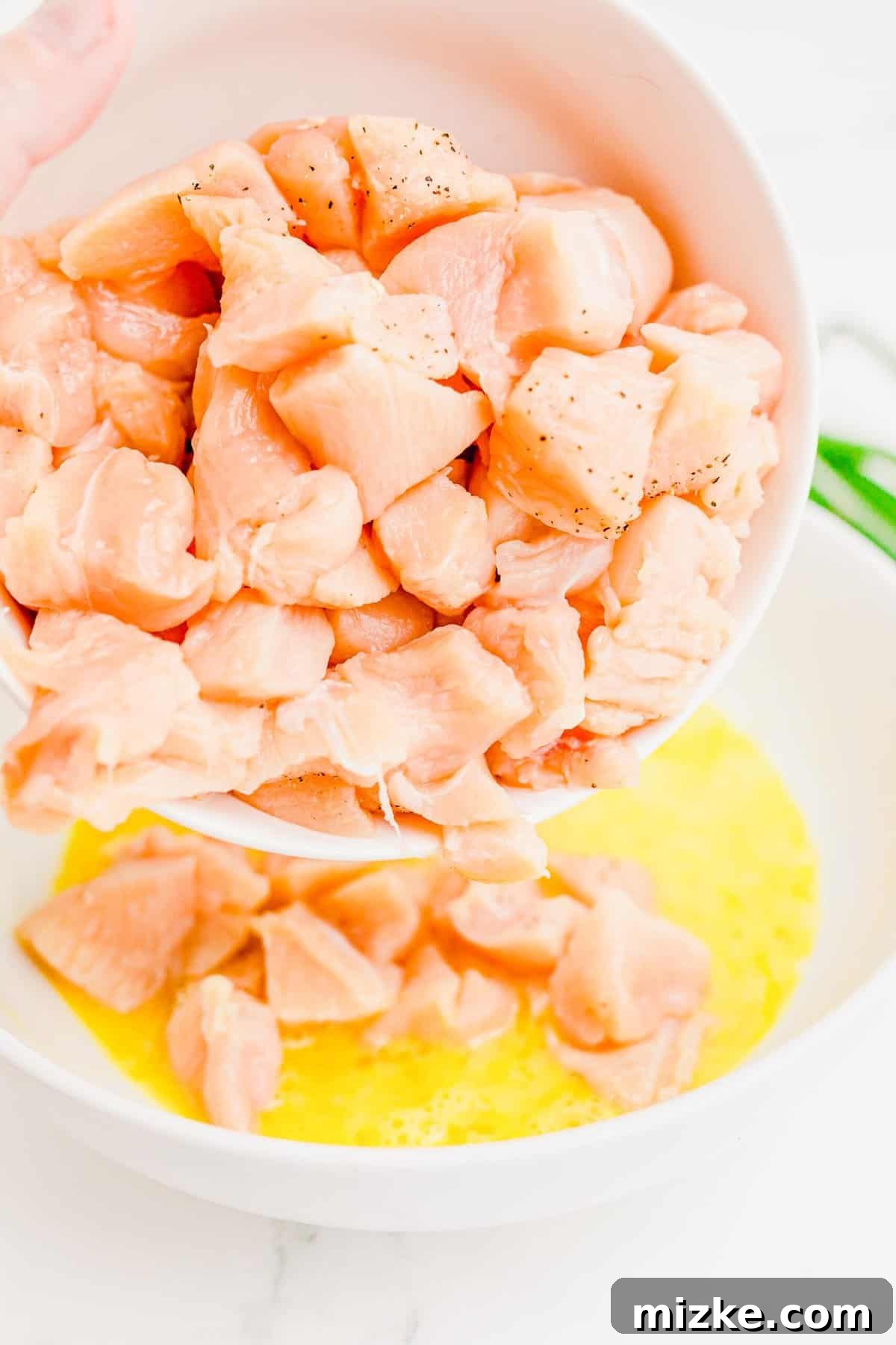Coating chicken in egg for a perfectly crisp crust. Raw chicken pieces being dipped and coated in beaten egg in a shallow bowl.