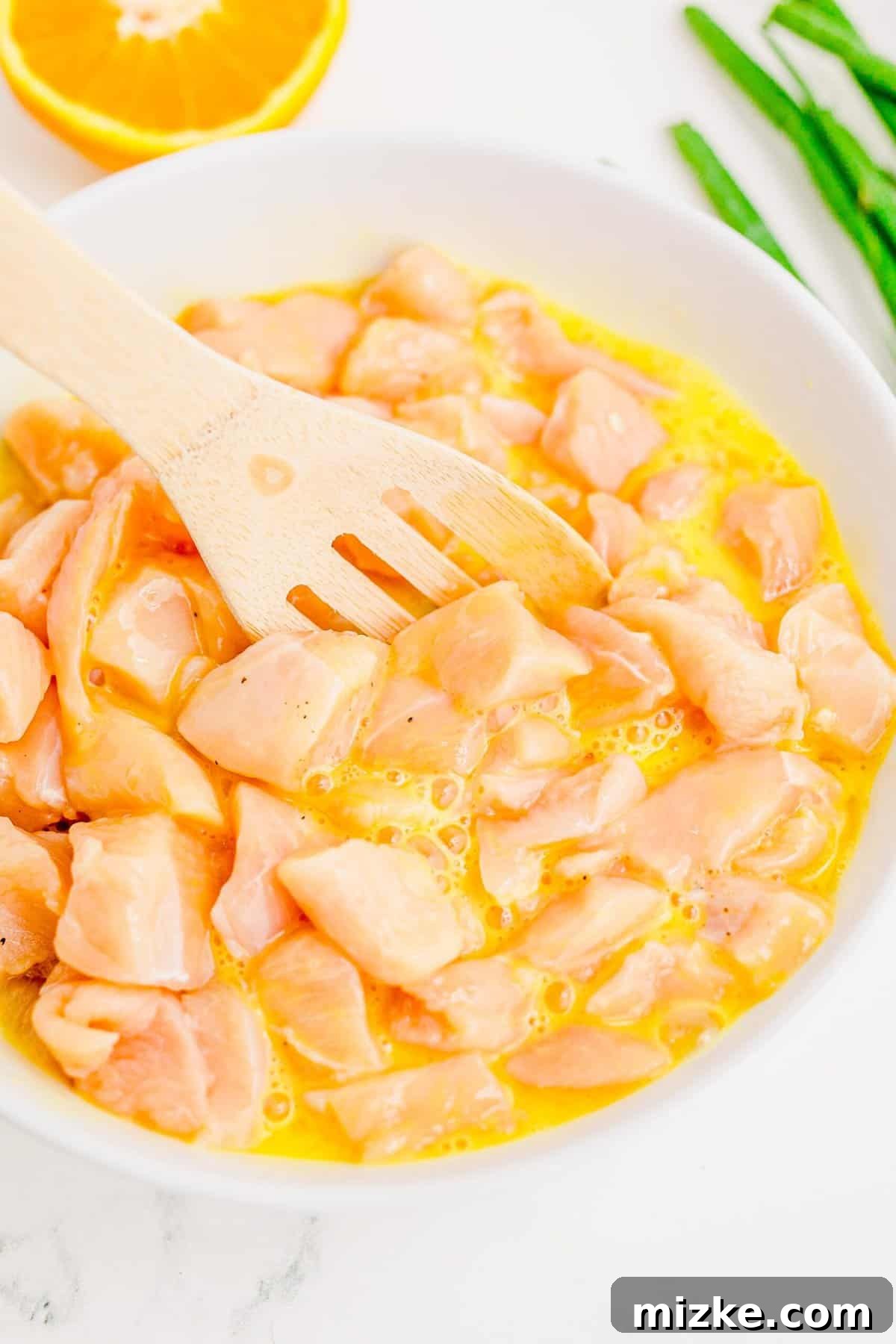 Ensuring every chicken piece is well-coated with egg before breading. Close-up of raw chicken thoroughly mixed with egg mixture in a bowl.