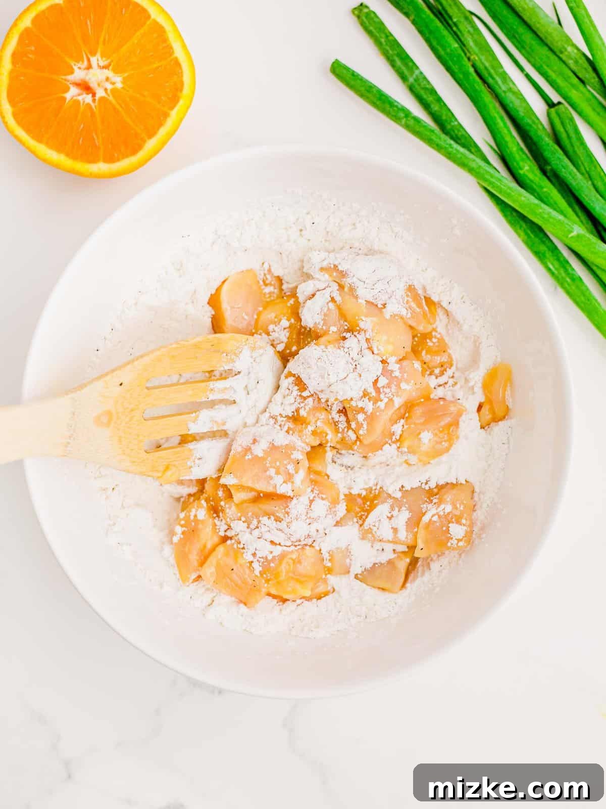 Achieving a complete and even breading on each chicken piece. Egg-dipped chicken being tossed and coated in a bowl of flour mixture.