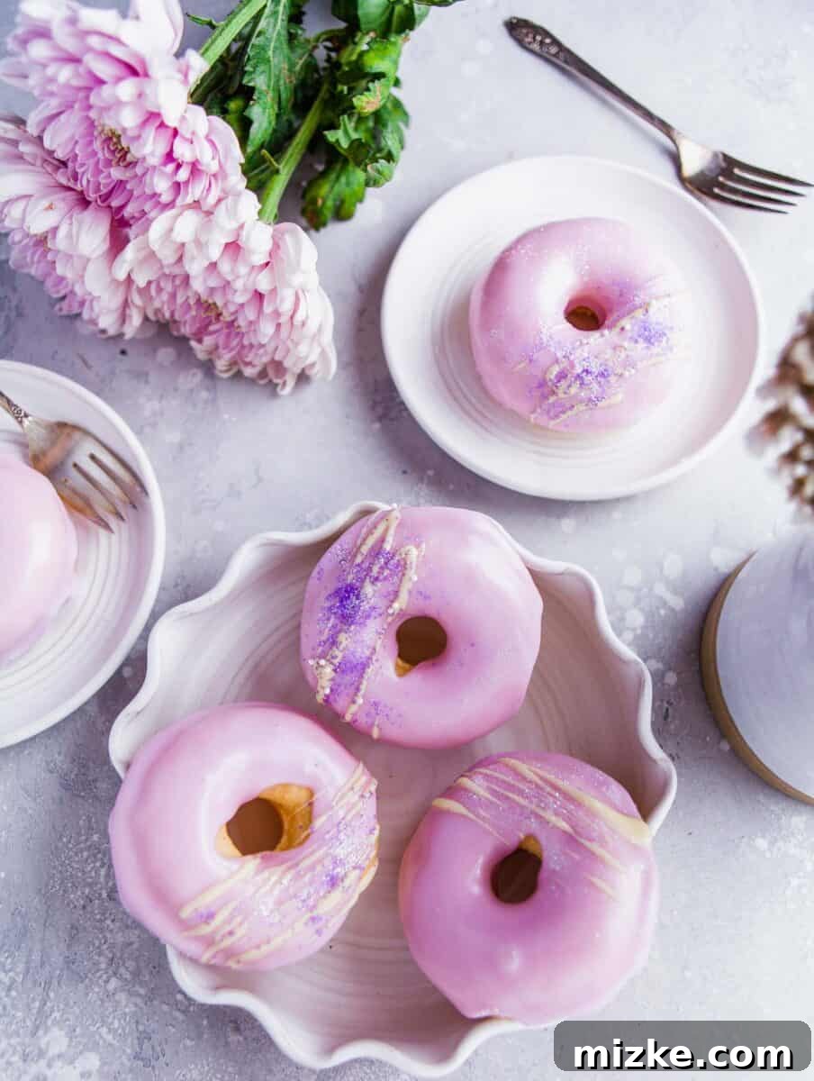 Perfectly Baked Vanilla Delights 2 Several baked and frosted vanilla donuts are artfully arranged on various white plates, showcasing their beautiful frosting colors and sprinkles.