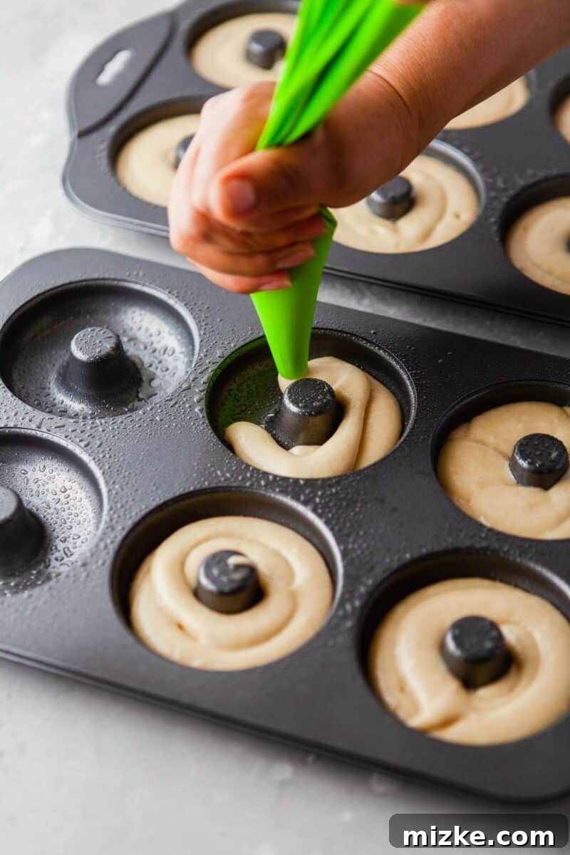 Perfectly Baked Vanilla Delights 6 Smooth donut batter is being expertly piped into the cavities of a donut baking pan, ensuring even filling.