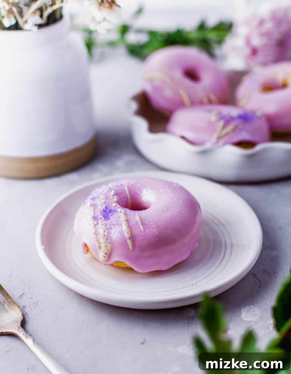 Perfectly Baked Vanilla Delights 9 A single perfectly round pink frosted donut, with delicate sprinkles, is presented on a pristine white plate.