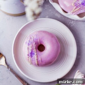 A frosted vanilla donut with a white chocolate drizzle, placed on a round white plate, ready to be enjoyed.