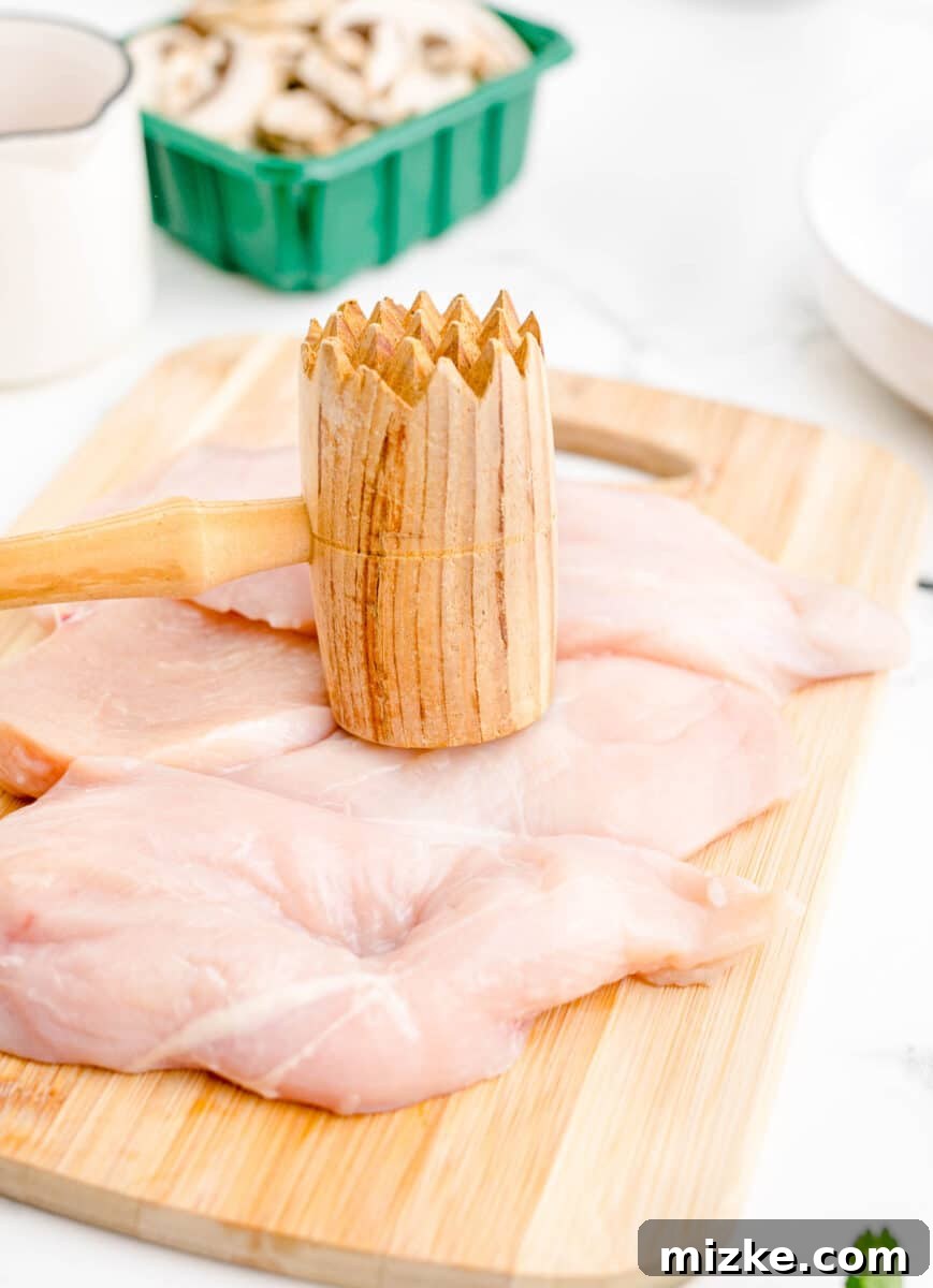 Simple Weeknight Chicken Marsala 4 A chicken breast is being carefully pounded with a wooden mallet on a cutting board, preparing it for cooking.